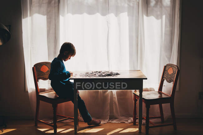 Мальчик, сидящий за столом и собирающий пазл — стоковое фото