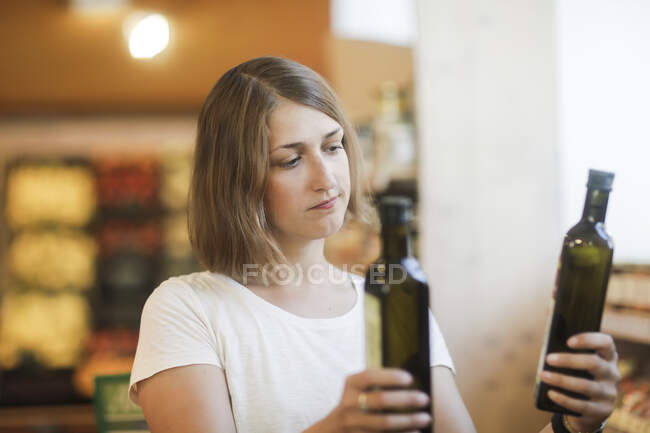 Woman standing in a supermarket comparing bottles of olive oil — Stock Photo