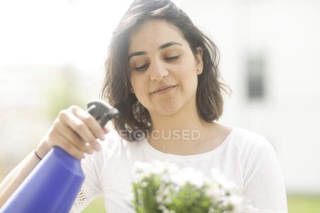 Woman standing in garden spraying pot plant — Stock Photo