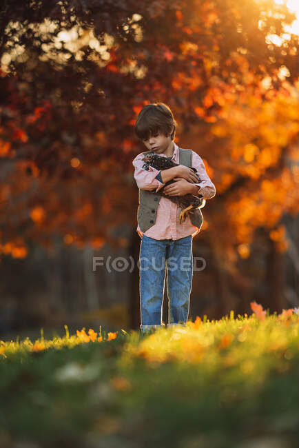 Niño parado al aire libre abrazando a un pollo, Estados Unidos - foto de stock