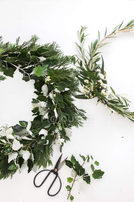 Ciseaux et couronne de Noël sur table blanche — Photo de stock