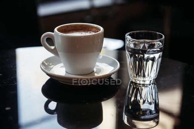 Primer plano de una taza de café y un vaso de agua sobre una mesa - foto de stock