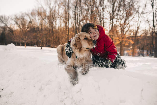 Rapaz abraçando seu cão golden retriever na neve — Fotografia de Stock