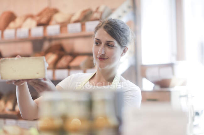 Sales assistant standing in a supermarket holding a piece of cheese — Stock Photo