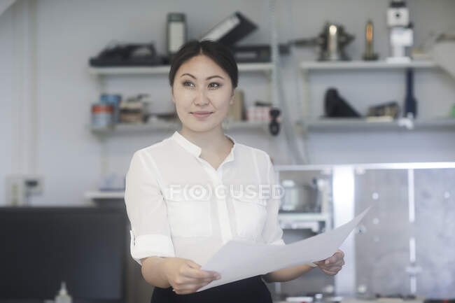Smiling Female engineer standing in a workshop looking at technical drawings — Stock Photo