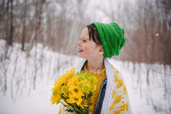 Sorrindo Menina de pé na neve segurando um monte de flores — Fotografia de Stock