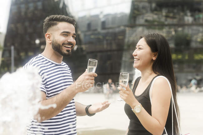 Couple standing by a water fountain making a celebratory toast — Stock Photo