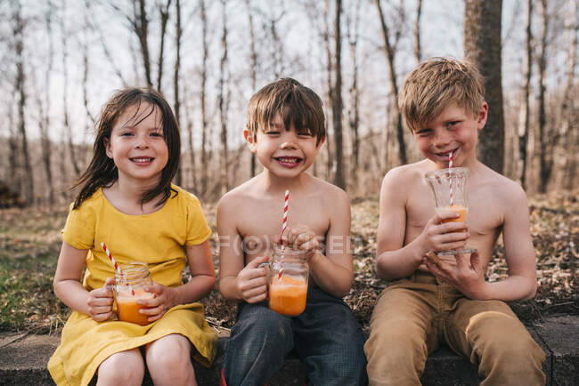 Tre bambini seduti su un muro a godersi le bevande estive — Foto stock