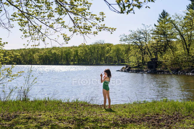 Mädchen steht im Badeanzug am See und setzt ihre Sonnenbrille auf — Stockfoto