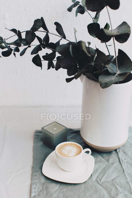 Copa de café junto a un jarrón y una vela - foto de stock