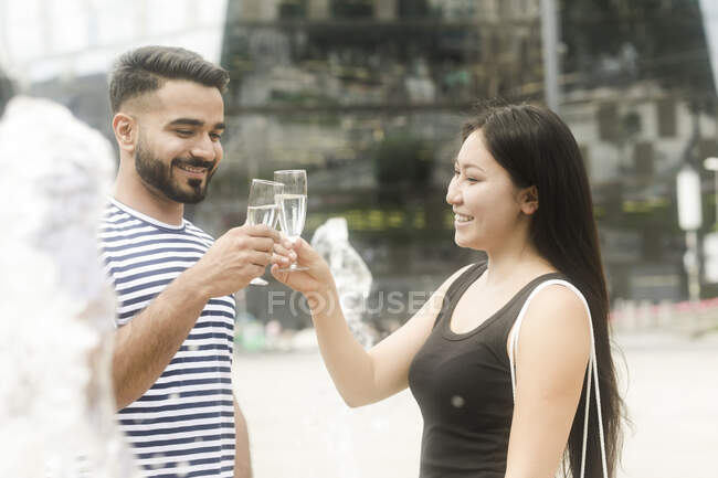 Couple standing by a water fountain making a celebratory toast — Stock Photo