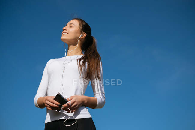 Smiling woman standing outdoors listening to music — Stock Photo