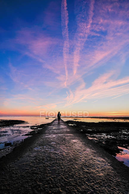 Силуэт женщины, стоящей на пристани у моря, фиолетовое небо заката — стоковое фото