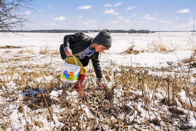 Garçon sur une chasse aux œufs de Pâques dans la neige — Photo de stock