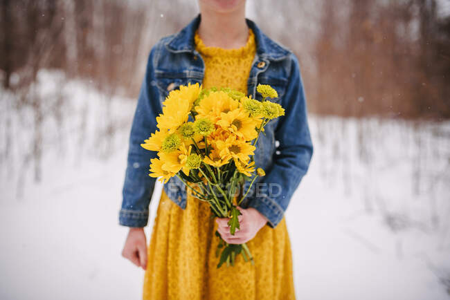 Close-up de uma menina de pé na neve segurando um monte de flores — Fotografia de Stock