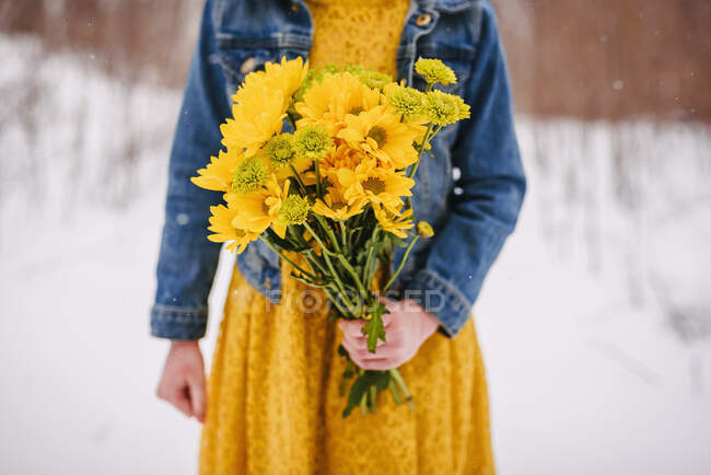 Gros plan d'une fille debout dans la neige tenant un bouquet de fleurs — Photo de stock
