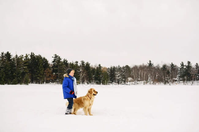 Ragazzo a piedi il suo cane nella neve sulla natura — Foto stock