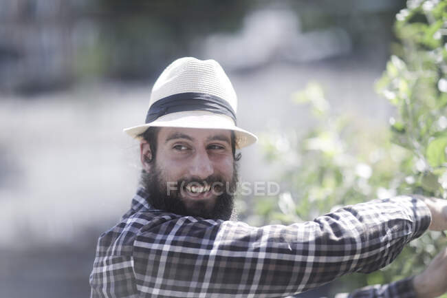 Uomo sorridente in piedi nel giardino potatura di un arbusto — Foto stock