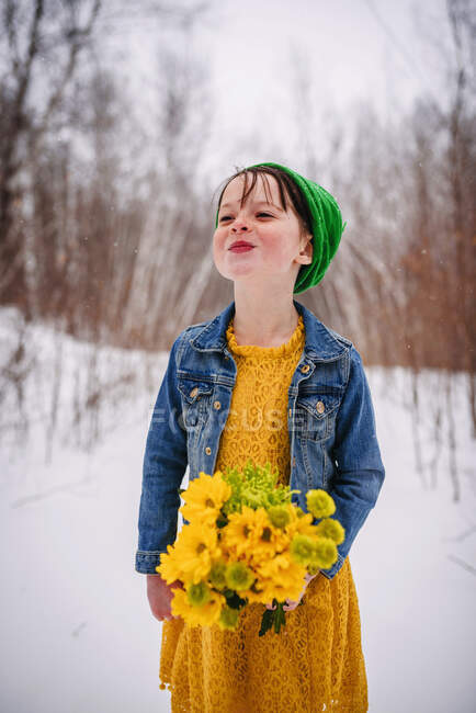 Menina de pé na neve segurando um monte de flores — Fotografia de Stock