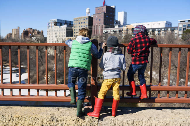 Трое детей стоят на мосту Стоун Арч и смотрят на городской пейзаж, Миннеаполис, Миннесота, Америка, США — стоковое фото