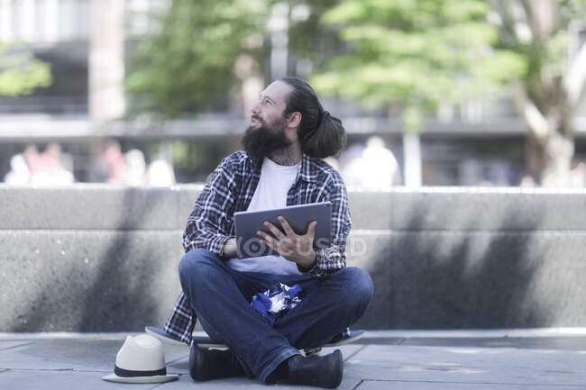 Чоловік сидить на скейтборді за допомогою цифрового планшета — стокове фото