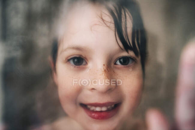 Portrait of a smiling girl looking through the wet shower glass — Stock Photo
