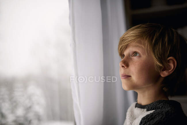 Мальчик зимой смотрит в окно — стоковое фото