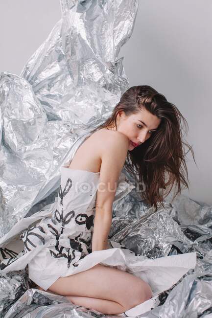 Женщина в бумажном платье сидит на серебряной фольге — стоковое фото