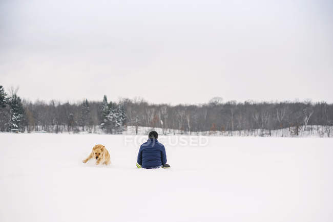 Hombre y perro jugando en la nieve - foto de stock