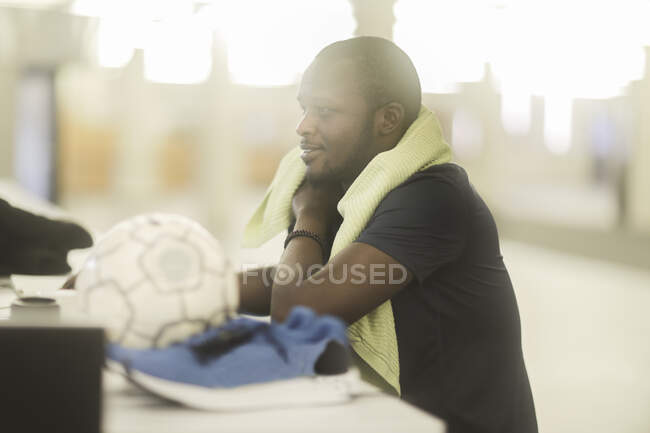 Hombre sentado en un escritorio con un balón de fútbol y entrenadores a su lado - foto de stock