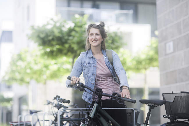 Усміхнена жінка стоїть поруч з електричним велосипедом — стокове фото