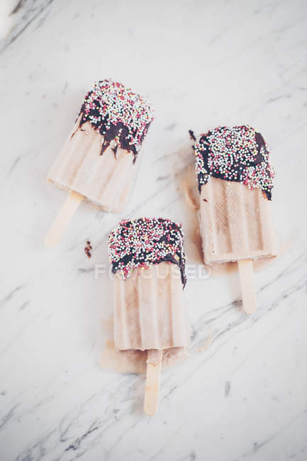 Three yogurt ice-creams dipped in chocolate and sprinkles — Stock Photo