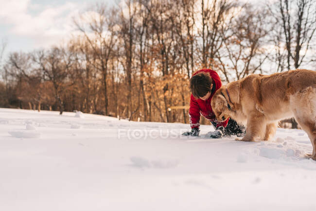 Menino brincando na neve com seu cão golden retriever — Fotografia de Stock