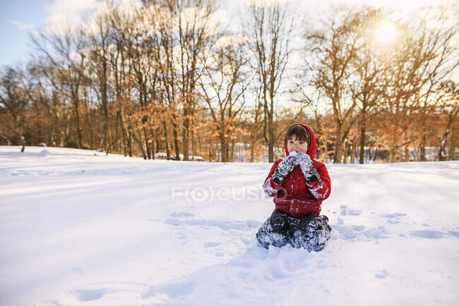 Boy sitting in the garden eating snow — Stock Photo
