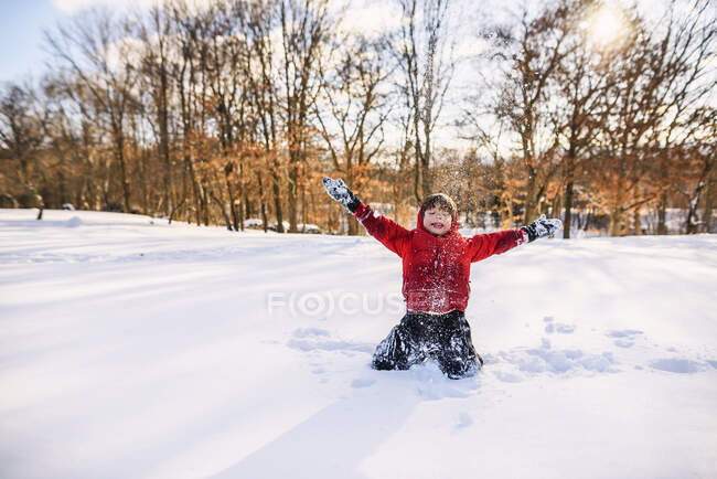 Мальчик сидит в снегу с поднятыми руками — стоковое фото