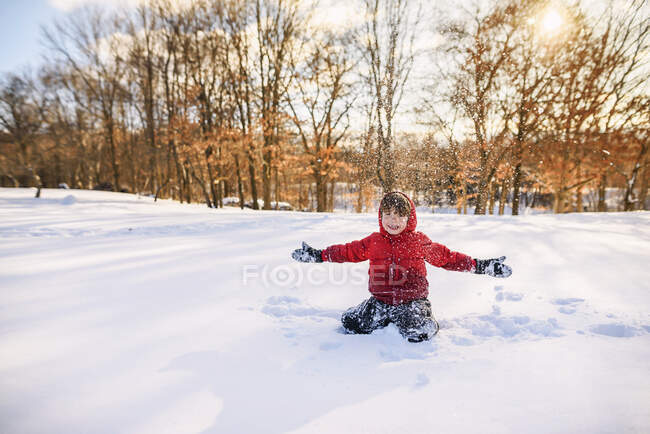 Мальчик сидит в снегу с протянутыми руками — стоковое фото