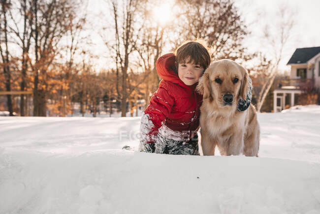 Retrato de un niño sentado en la nieve con su perro golden retriever - foto de stock