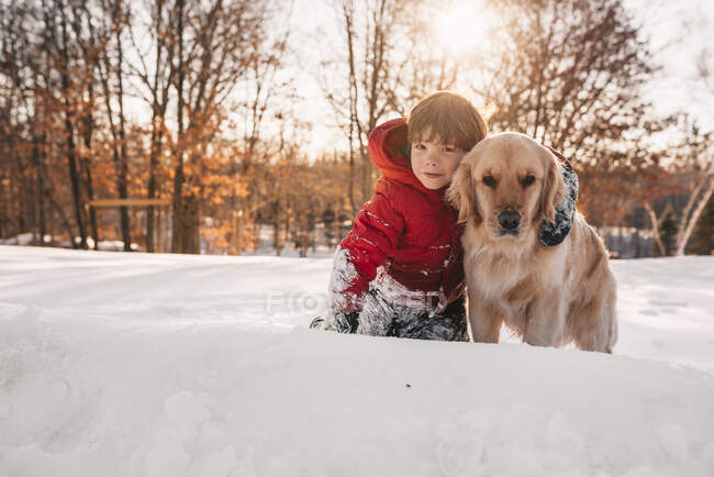 Portrait of a boy sitting in snow with his golden retriever dog — Stock Photo