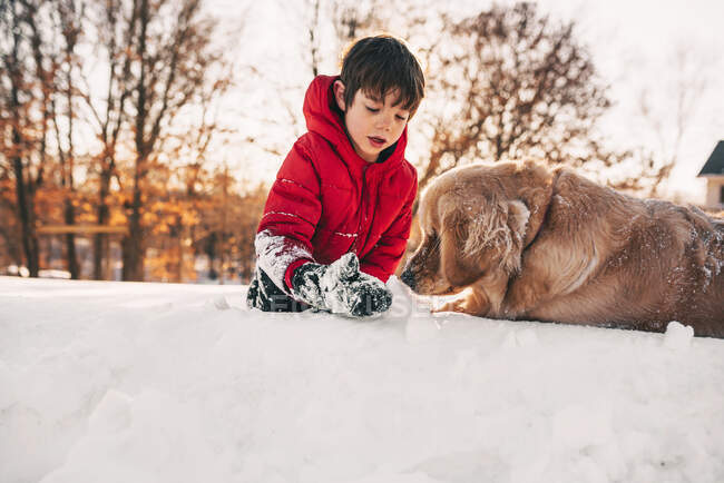 Garçon jouant dans la neige avec son chien golden retriever — Photo de stock