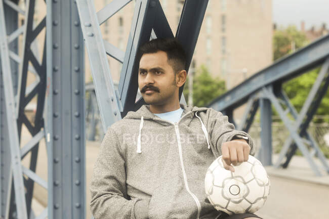 Uomo seduto su una passerella con in mano un pallone da calcio — Foto stock