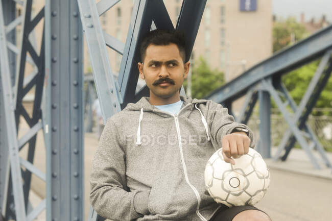 Homme assis sur une passerelle tenant un ballon de football — Photo de stock