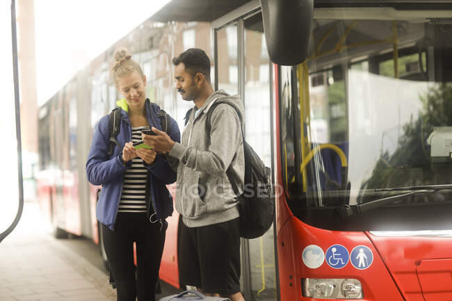 Coppia in piedi vicino a un autobus guardando un telefono cellulare — Foto stock