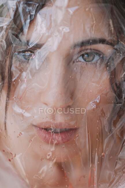 Femme regardant à travers plastique transparent humide sur fond blanc — Photo de stock
