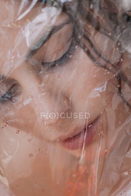 Mulher olhando através de plástico transparente molhado no fundo branco — Fotografia de Stock