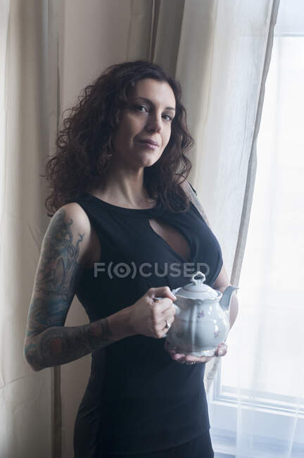 Frau steht am Fenster und hält eine Teekanne — Stockfoto