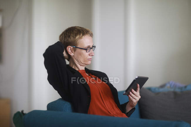 Жінка сидить на дивані за допомогою цифрового планшета — стокове фото