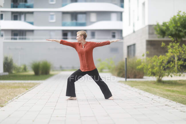 Woman standing outside doing yoga warrior pose — Stock Photo