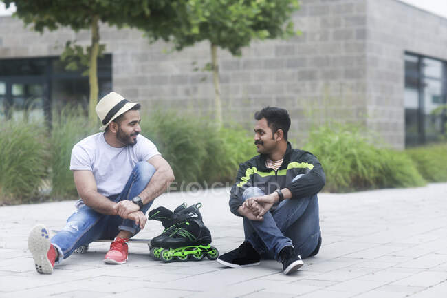 Two men sitting outdoors with a skateboard and rollerblades — Stock Photo