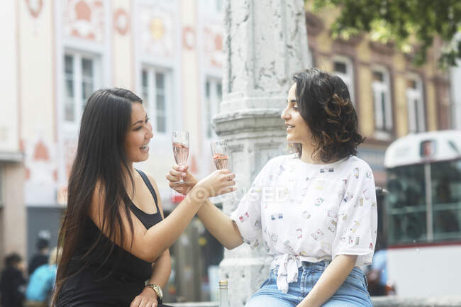 Two women sitting by a water fountain making a celebratory toast — Stock Photo