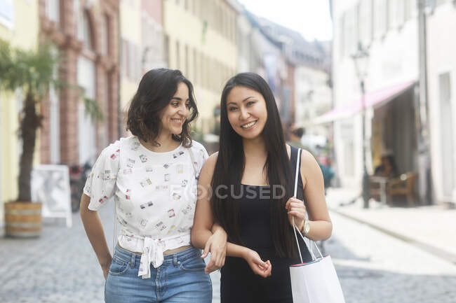 Retrato de dos mujeres caminando brazo en brazo por la calle - foto de stock